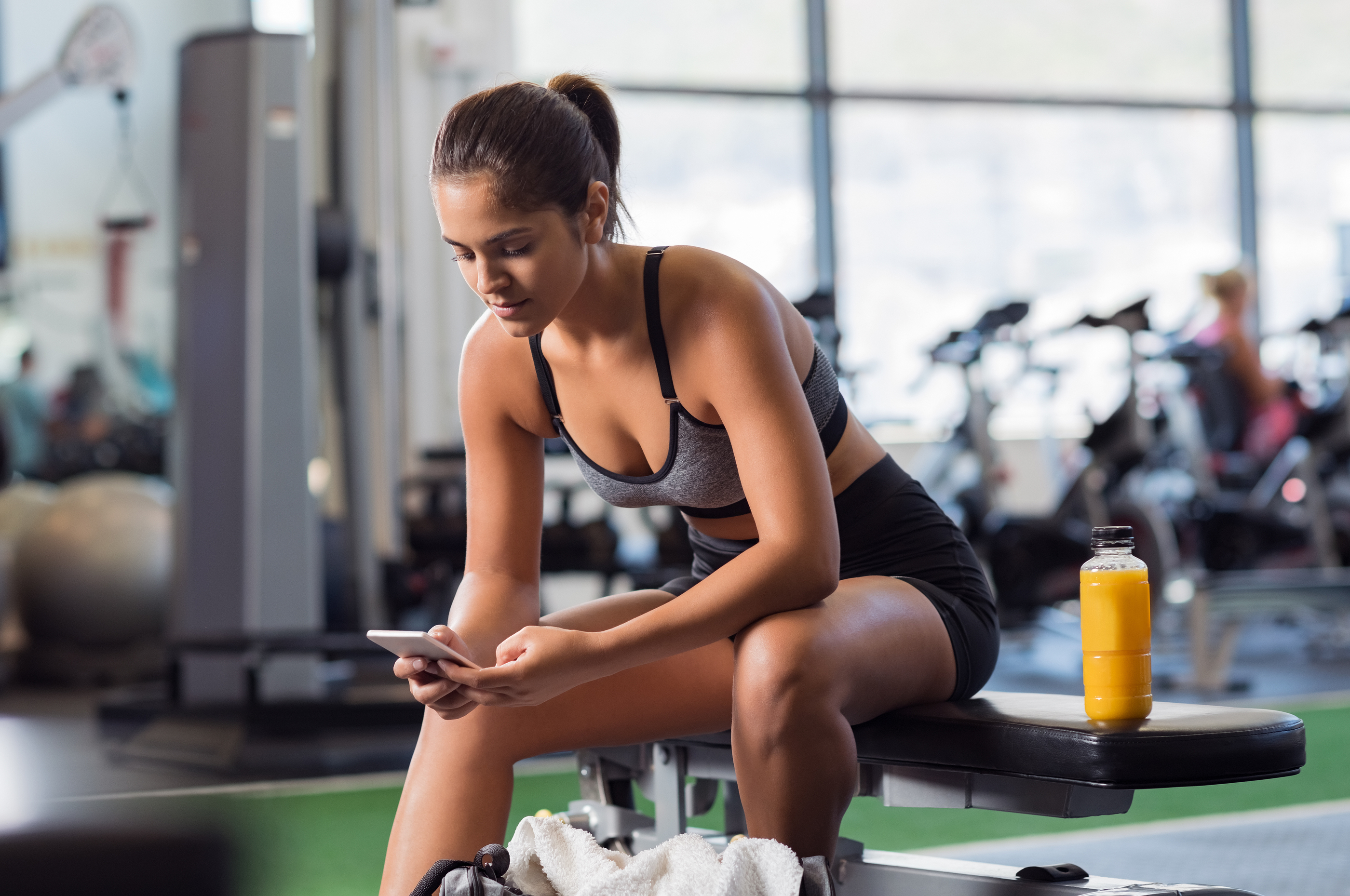 Young woman athlete using cell phone at gym. Latin woman in spor